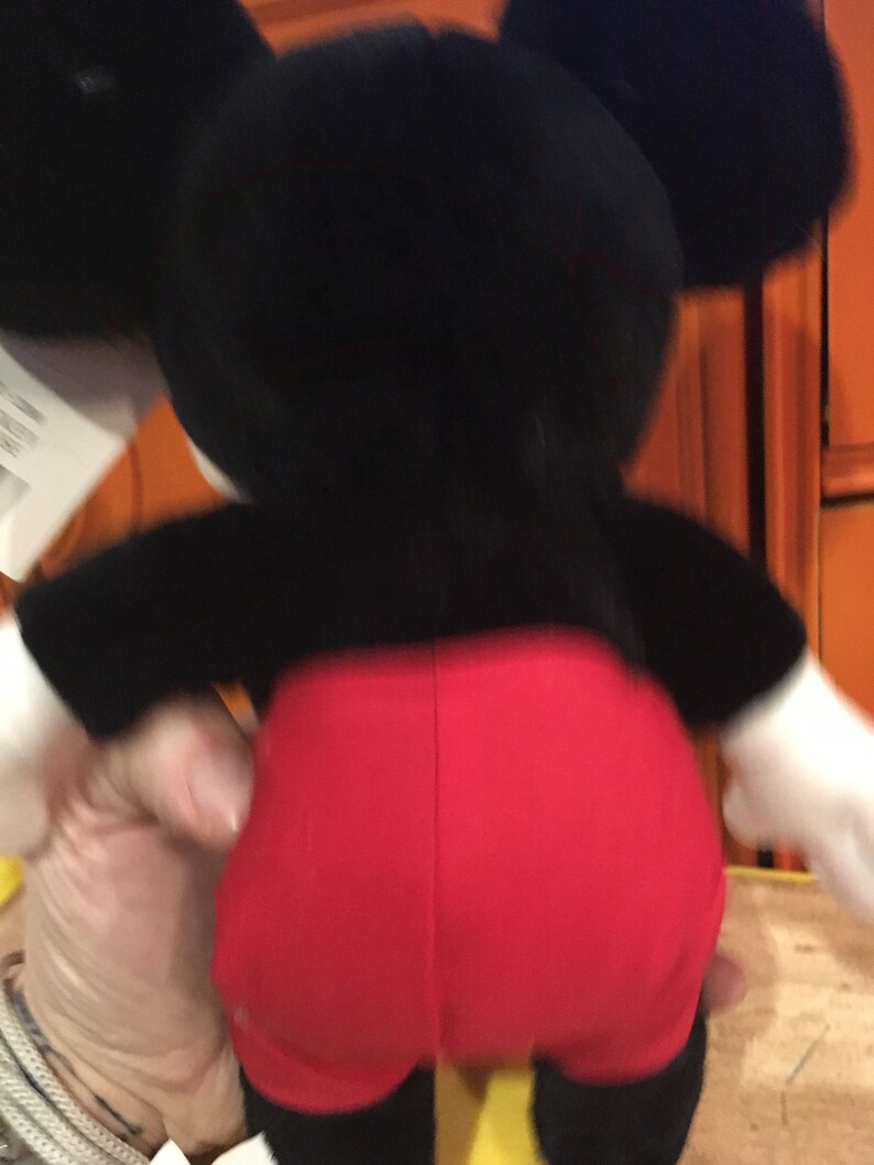 Puede incluir: Un juguete de peluche Mickey Mouse negro y rojo. El juguete est&aacute; de pie sobre una superficie amarilla.