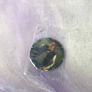 Può includere: Una moneta rotonda di colore argentato con l'immagine di un uomo con una camicia bianca e una giacca nera. L'uomo guarda di lato e ha un'espressione seria sul viso.