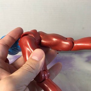 Puede incluir: Una figura de acci&oacute;n de pl&aacute;stico rojo con pelo azul, posada en una posici&oacute;n doblada con un brazo extendido. La figura tiene articulaciones.