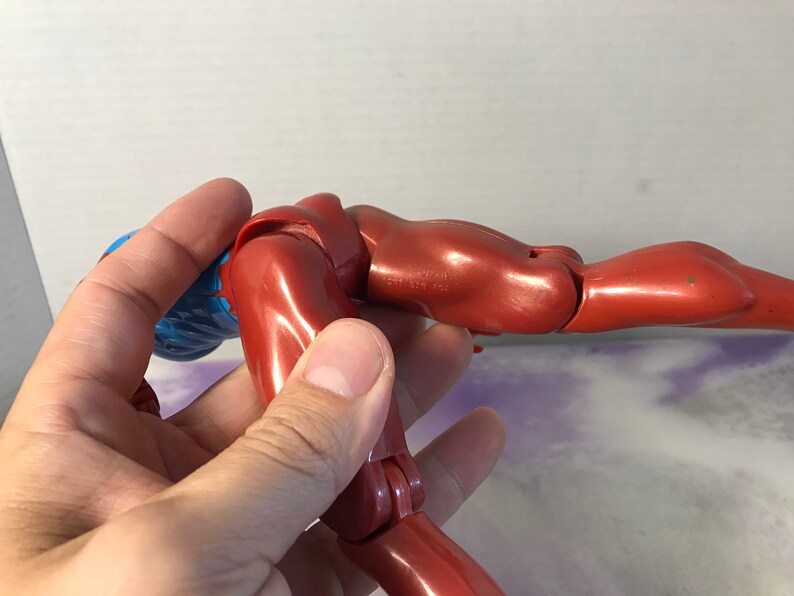 Puede incluir: Una figura de acci&oacute;n de pl&aacute;stico rojo con pelo azul, posada en una posici&oacute;n doblada con un brazo extendido. La figura tiene articulaciones.
