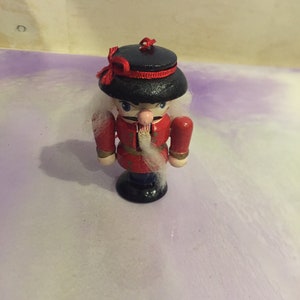 May include: A wooden nutcracker ornament with a red and black uniform, white beard, and a black hat with a red ribbon.
