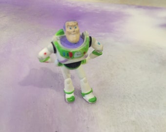 May include: A white and green plastic toy action figure of Buzz Lightyear from the Toy Story movie franchise. The figure has a purple chest piece and a green visor.