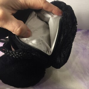 Puede incluir: Bolso de peluche negro con cierre de cremallera y asa de cord&oacute;n trenzado.