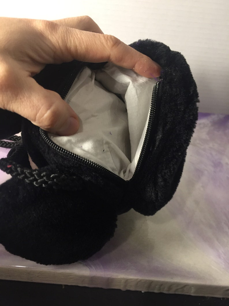 Puede incluir: Bolso de peluche negro con cierre de cremallera y asa de cord&oacute;n trenzado.