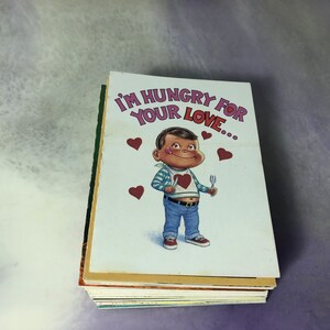 May include: A stack of greeting cards with a cartoon illustration of a person holding a knife and fork. The card reads "I'm hungry for your love..."