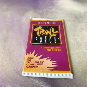 May include: A purple and yellow card pack for a collectible card game called "Troll Force". The pack includes 7 collectible cards and 1 sticker. The text on the pack says "Look for Troll Force comic strip cards!"