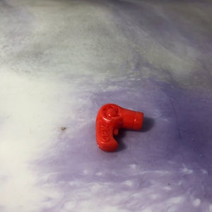 May include: A red plastic toy hairdryer. The hairdryer has a black button and a white nozzle.