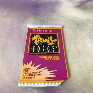 May include: A purple and yellow card pack with the text "TROLL FORCE" in a black and white graphic font. The pack contains 7 collectible cards and 1 sticker. The text "LOOK FOR TROLL FORCE™ COMIC STRIP CARDS!!!" is printed on the bottom of the pack.
