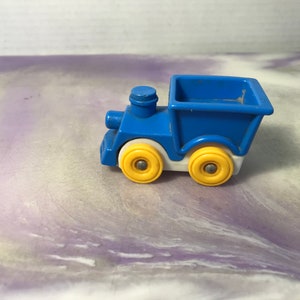 May include: A blue toy train with a white cab and yellow wheels. The train has a blue dump bed.
