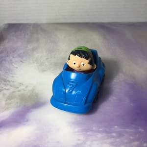 May include: A blue toy car with a cartoon character driver wearing a green hat. The car has a number "7" on the side.
