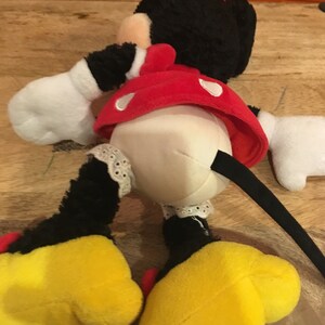 Op de afbeelding: Een pluche Minnie Mouse speelgoed in zwart en rood met gele schoenen en een zwarte staart. Het speelgoed draagt een rode jurk met witte stippen en een wit onderrokje met kant.