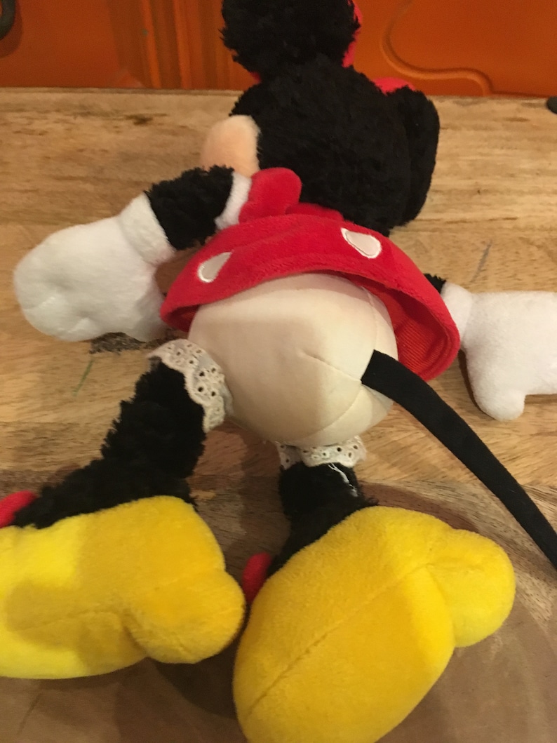 Op de afbeelding: Een pluche Minnie Mouse speelgoed in zwart en rood met gele schoenen en een zwarte staart. Het speelgoed draagt een rode jurk met witte stippen en een wit onderrokje met kant.