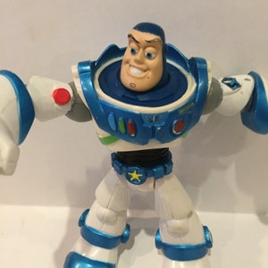 Pu&ograve; includere: Una action figure di Buzz Lightyear blu e bianca con una stella sulla cintura. La figura ha una testa rotante ed &egrave; in posizione eretta.