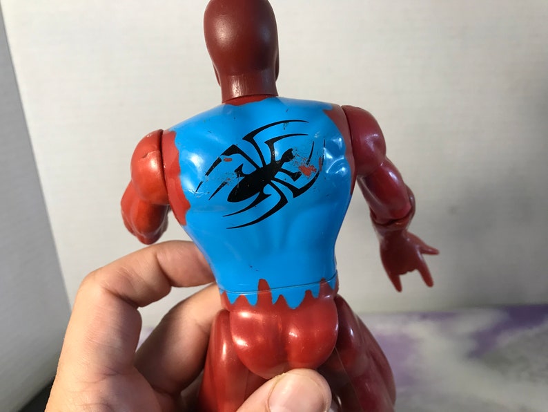 Puede incluir: Figura de acci&oacute;n roja y azul con un dise&ntilde;o de ara&ntilde;a negra en la espalda. La figura tiene una cabeza y un torso rojos, brazos y piernas azules, y un dise&ntilde;o de ara&ntilde;a negra en la espalda.