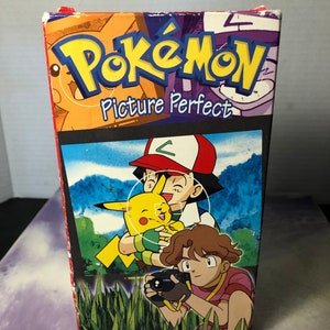May include: A VHS tape case featuring the Pokemon characters Pikachu, Ash, and Misty. The case is red, yellow, and blue with the words "Pokemon Picture Perfect" printed on the front.