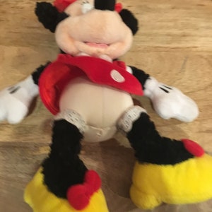 Op de afbeelding: Een pluche speelgoed van Minnie Mouse met een rode jurk met witte stippen en gele schoenen met rode strikken.