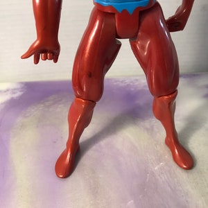 Puede incluir: Primer plano de las piernas de una figura de acci&oacute;n de pl&aacute;stico rojo. La figura tiene un torso rojo y azul y est&aacute; posada con una pierna doblada en la rodilla.