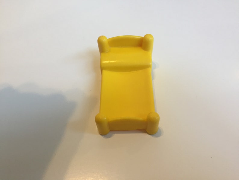 May include: A yellow plastic toy bed with rounded edges and four legs.
