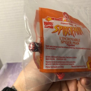 Puede incluir: Una figura de Spider-Man roja y azul en una bolsa de pl&aacute;stico con un empaque de juguete Happy Meal de McDonald's. El empaque presenta el logotipo de Marvel Comics y el texto "Joyeux f&ecirc;ter de Spider-Man L'Incroyable Spider-Man Figurine".