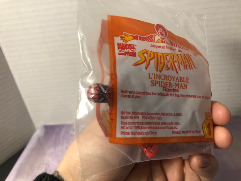 Puede incluir: Una figura de Spider-Man roja y azul en una bolsa de pl&aacute;stico con un empaque de juguete Happy Meal de McDonald's. El empaque presenta el logotipo de Marvel Comics y el texto "Joyeux f&ecirc;ter de Spider-Man L'Incroyable Spider-Man Figurine".