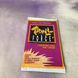 May include: A purple, yellow, and white card pack for Troll Force collectible cards. The pack features the text "STAR PICS PRESENTS" and "TROLL FORCE" in a bold, stylized font. The pack also includes the text "7 COLLECTIBLE CARDS PLUS 1 STICKER" and "LOOK FOR TROLL FORCE™ COMIC STRIP CARDS!!!".