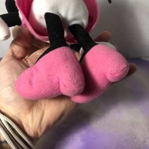 K&ouml;nnte beinhalten: Rosa und schwarzes Pl&uuml;schtier mit wei&szlig;em K&ouml;rper und schwarzen Beinen. Das Spielzeug tr&auml;gt ein rosa Kleid mit wei&szlig;en Punkten und einer schwarzen Schleife.