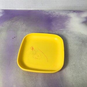 Könnte beinhalten: Ein quadratischer, gelber Teller aus Plastik mit einer roten Markierung auf der Oberfläche.