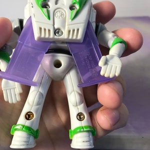 May include: A white and green Buzz Lightyear action figure with purple wings. The figure has a light blue helmet and is posed with its arms outstretched.
