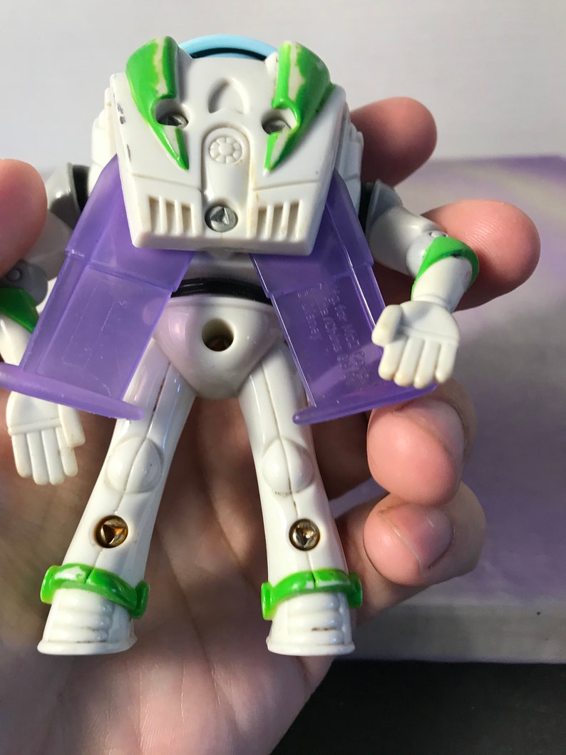 May include: A white and green Buzz Lightyear action figure with purple wings. The figure has a light blue helmet and is posed with its arms outstretched.