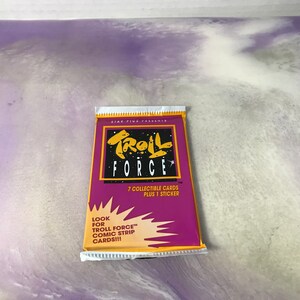 May include: A purple and yellow package of Troll Force trading cards. The package features the text "Troll Force" in a bold, stylized font. The package includes 7 collectible cards and 1 sticker. The text "Look for Troll Force Comic Strip Cards!!!" is printed on the package.
