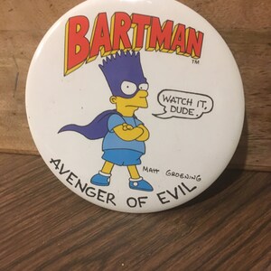 May include: A white button featuring a cartoon image of Bart Simpson dressed as a superhero. The button reads "Bartman" in red letters, "Avenger of Evil" in black letters, and "Watch it, dude." in a speech bubble. The button is signed "Matt Groening".