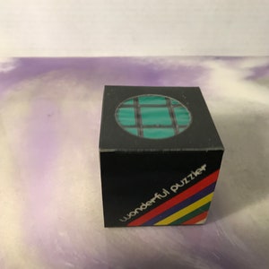 Może przedstawiać: Czarne pudełko z zielono-czarną układanką w środku. Na pudełku widnieje napis "wonderful puzzle".