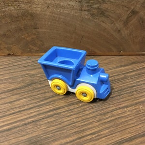 May include: A blue toy train with yellow wheels. The train has a white cab and a blue cargo car.