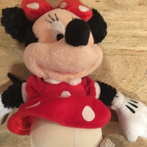 Op de afbeelding: Een pluche speelgoed van Minnie Mouse met een rode jurk met witte stippen en een rode strik met witte stippen.