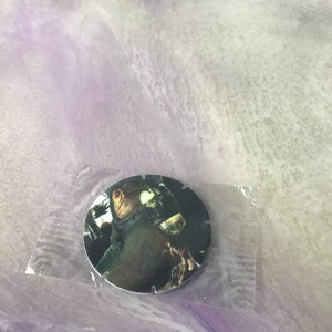 Può includere: Un disco da collezione rotondo e scuro con una scena di un film, racchiuso in una custodia di plastica trasparente. L'immagine sul disco raffigura un personaggio in un'ambientazione scura. Il disco ha un bordo dentellato.