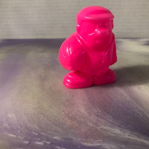 Könnte beinhalten: Eine rosafarbene Plastikfigur einer Person mit Hut und einem Ball in der Hand. Die Figur ist etwa 5 cm groß.