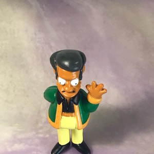 May include: A green and yellow plastic figurine of a cartoon character with a mustache and a black afro.