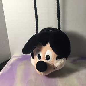 Puede incluir: Bolso de peluche negro con forma de cabeza de Mickey Mouse con una correa de cuerda negra.