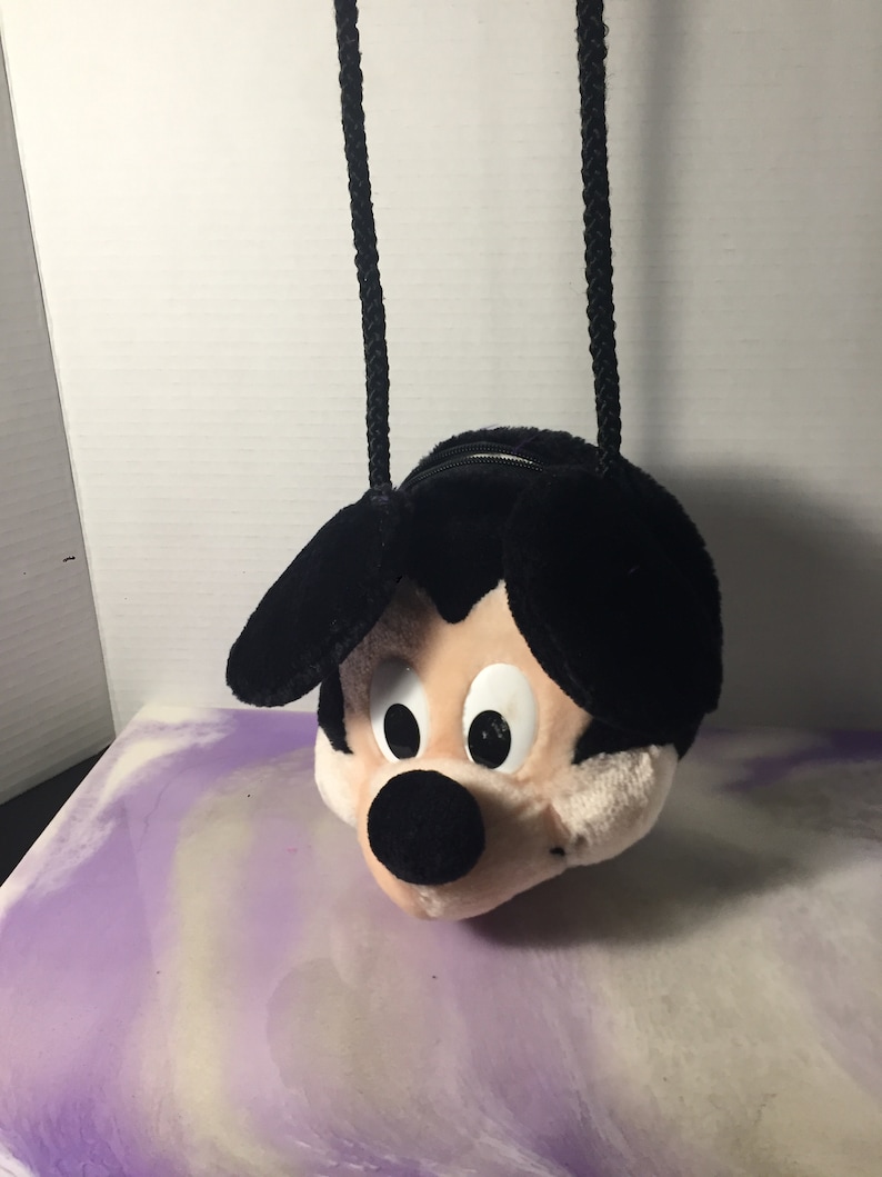 Puede incluir: Bolso de peluche negro con forma de cabeza de Mickey Mouse con una correa de cuerda negra.