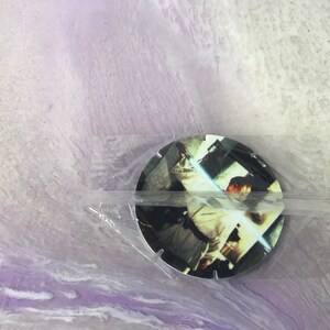 Può includere: Uno spillo rotondo, bianco e nero, a tema Star Wars con un personaggio che tiene una spada laser. Lo spillo è in una busta di plastica trasparente.