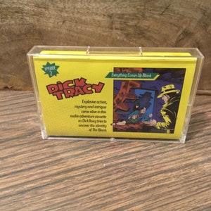 Peut inclure: Une cassette audio jaune avec une image de Dick Tracy sur le devant. Le texte sur la cassette indique "Episode 2 Everything Comes Up Blank". Le texte sous l'image indique "Action explosive, mystère et intrigue prennent vie dans cette cassette d'aventure audio alors que Dick Tracy tente de découvrir l'identité de The Blank."