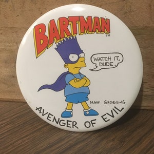 May include: A white round button with a cartoon image of Bart Simpson dressed as a superhero. The button says "Bartman" in red letters, "Avenger of Evil" in black letters, and "Watch it, dude." in a speech bubble. The button is signed "Matt Groening".