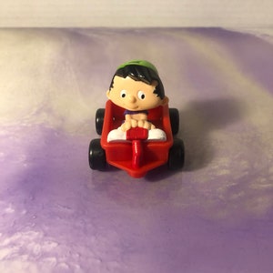 May include: A red toy wagon with a small cartoon figure of a boy wearing a green hat and a purple shirt. The boy is sitting in the wagon and holding the handle.
