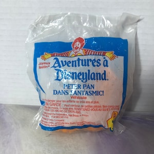 May include: A blue and orange plastic bag with a cartoon character on the front. The bag says "Aventures à Disneyland" and "Peter Pan dans Fantasmic!"  The bag is for a toy vehicle.