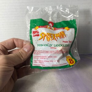 May include: A plastic bag containing a Happy Meal toy, a red and blue Spider-Man Hobgoblin Landglider vehicle. The bag is green and white with the words "Marvel Comics" and "Spider-Man" printed on it. The bag also has a number 8 printed on it.
