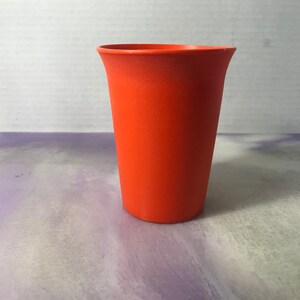 Könnte beinhalten: Ein leuchtend orangefarbener Plastikbecher mit einer glatten, abgerundeten Oberfläche.