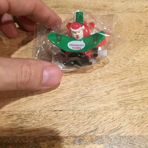 May include: A red and green wind-up toy of Santa Claus on a plane with the words "Merry Christmas" on the plane's wing.