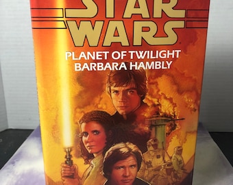 May include: A paperback book cover for the Star Wars novel "Planet of Twilight" by Barbara Hambly. The cover features a colorful illustration of Luke Skywalker, Princess Leia, and Han Solo.