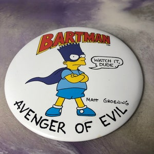 May include: A white round button featuring a cartoon image of Bart Simpson dressed as a superhero. The text on the button reads "Bartman, Avenger of Evil, Watch it, Dude, Matt Groening".