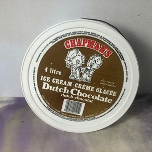 May include: A white plastic tub with a brown label. The label features a cartoon illustration of two children holding ice cream cones. The label reads "Chapman's 4 litre Ice Cream - Crème Glacée Dutch Chocolate dutch chocolat".